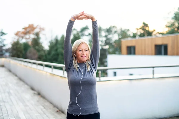 En äldre kvinna som motionerar utomhus, stretchar. — Stockfoto