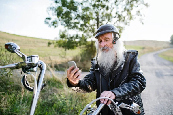 Un hombre mayor viajero con moto en el campo, tomando selfie . —  Fotos de Stock