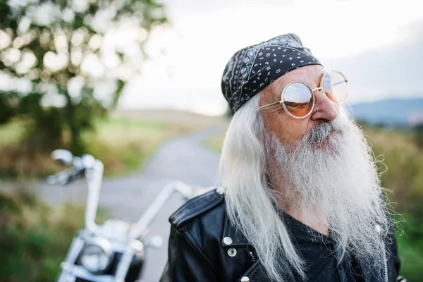 Starszy mężczyzna podróżnik z motocyklem i okularami przeciwsłonecznymi na wsi. — Zdjęcie stockowe