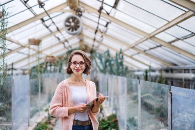 Young woman researcher standing in greenhouse, using tablet.