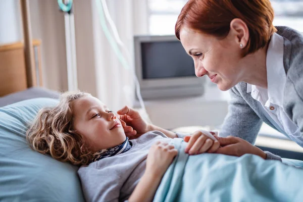 Caring mother visiting small girl daughter in bed in hospital. — Stock Photo, Image