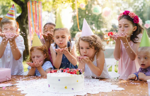 Enfants avec gâteau debout autour de la table à la fête d'anniversaire dans le jardin en été . — Photo