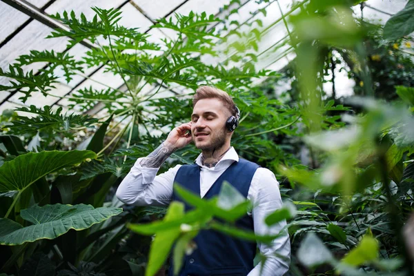 Young man with headphones standing in botanical garden. — Stock Photo, Image