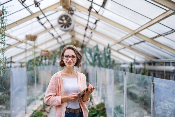 Young woman researcher standing in greenhouse, using tablet. — Stockfoto