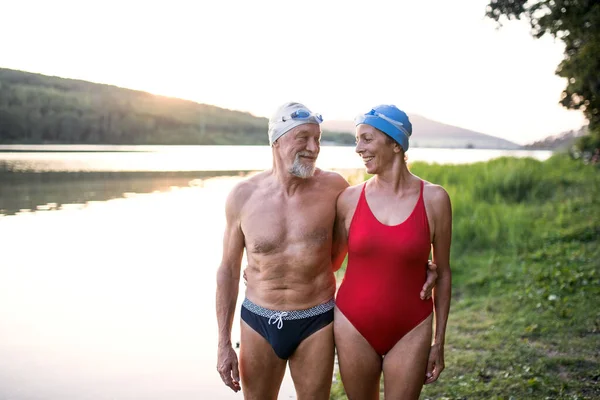 Casal sênior em maiô em pé junto ao lago ao ar livre antes de nadar . — Fotografia de Stock