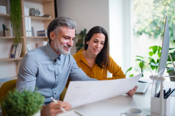 Architekten sitzen drinnen im Büro am Schreibtisch und betrachten Baupläne. — Stockfoto