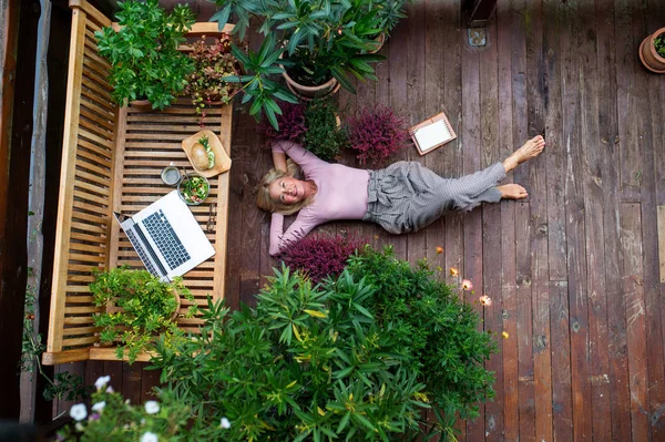 Visão superior da mulher sênior com laptop deitado ao ar livre no terraço, descansando . — Fotografia de Stock