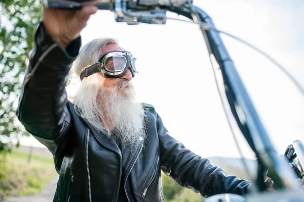 Ein älterer Mann mit Motorrad und Schutzbrille auf dem Land. — Stockfoto