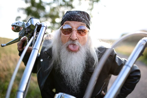 Senior man traveller with motorbike in countryside, having fun. — Stok fotoğraf