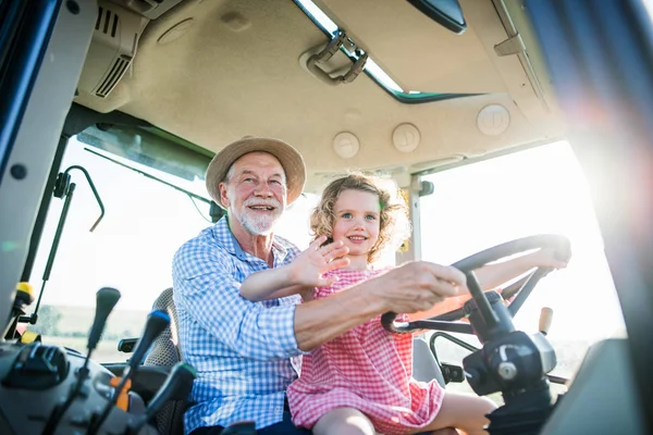 Starszy rolnik z małą wnuczką siedzi w ciągniku, jazdy. — Zdjęcie stockowe