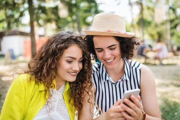 Portrait of two young women friends at summer festival, using smartphone. — ストック写真