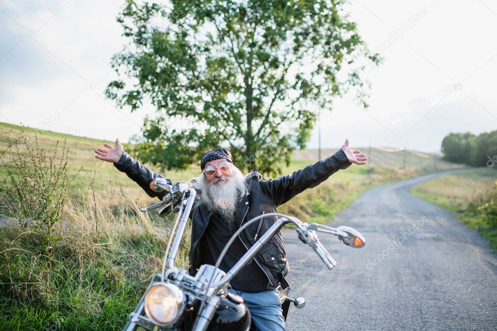 Senior man traveller with motorbike in countryside, stretching arms.