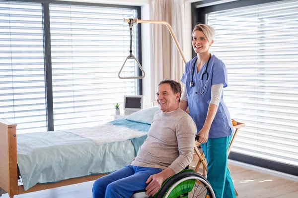 A healthcare worker and senior patient in wheelchair in hospital.