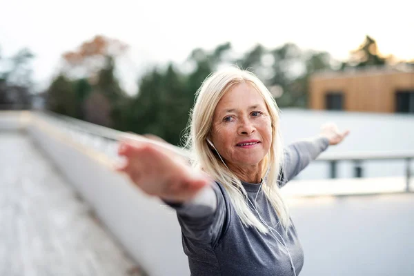 Una mujer mayor con auriculares al aire libre haciendo ejercicio . — Foto de Stock