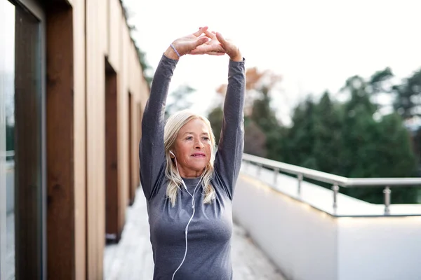 En äldre kvinna med hörlurar utomhus som motionerar. — Stockfoto