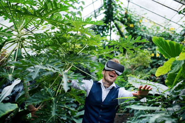 Frontansicht eines jungen Mannes, der im botanischen Garten steht und eine Vr-Brille benutzt. — Stockfoto