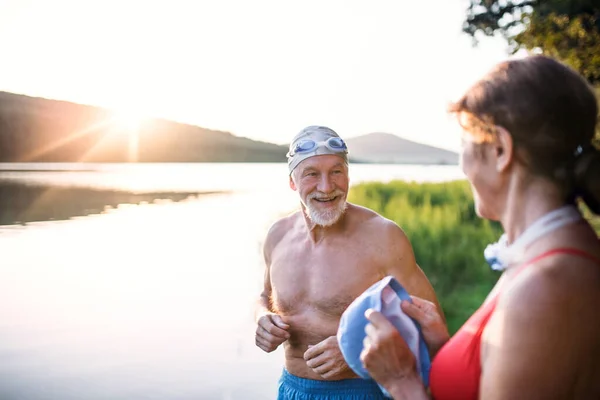 Pareja mayor en traje de baño de pie junto al lago al aire libre antes de nadar . —  Fotos de Stock