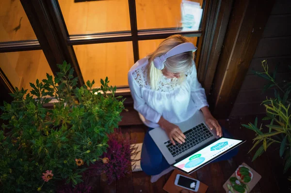 Senior woman with laptop sitting outdoors on terrace, working in the evening. — 图库照片