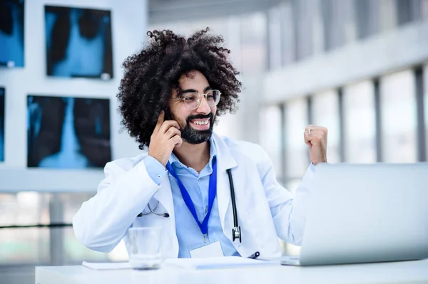 Portrét mužského lékaře sedícího v nemocnici, používajícího notebook a smartphone. — Stock fotografie