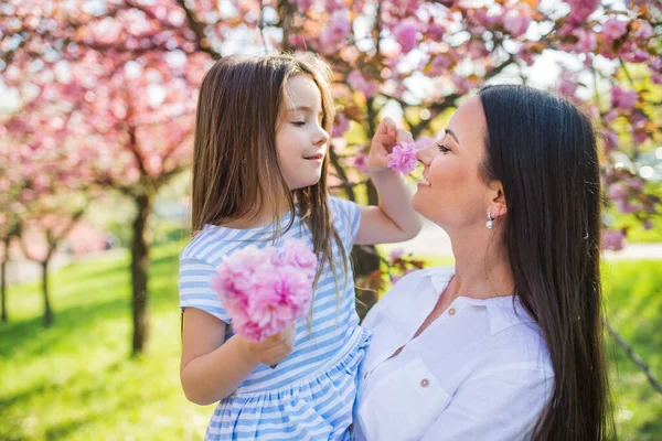 Young mother holding small daughter outside in spring nature. — Stock Photo, Image