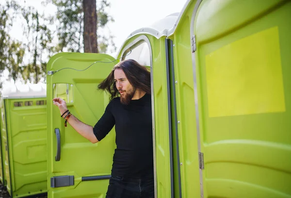 Young man by mobile toilet at summer festival. — Stock Photo, Image