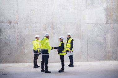 Group of engineers standing on construction site, shaking hands.