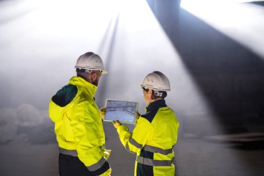Rear view of engineers standing on construction site, holding tablet.
