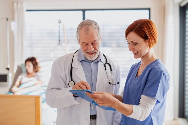 Portrait d'un médecin homme âgé debout dans une chambre d'hôpital, parlant à une infirmière . — Photo