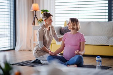 Healthcare worker and pregnant woman at home, doing yoga exercise.