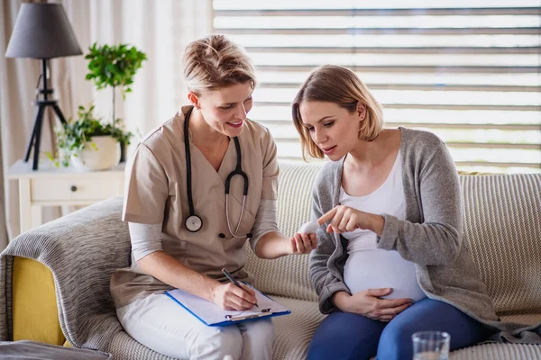 Una trabajadora de la salud examinando a una mujer embarazada en casa . — Foto de Stock
