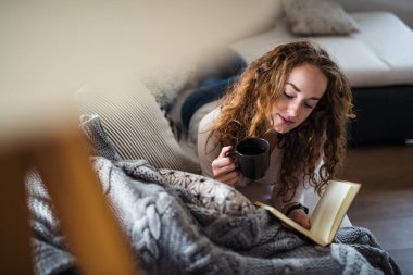 Young woman relaxing indoors at home with book.