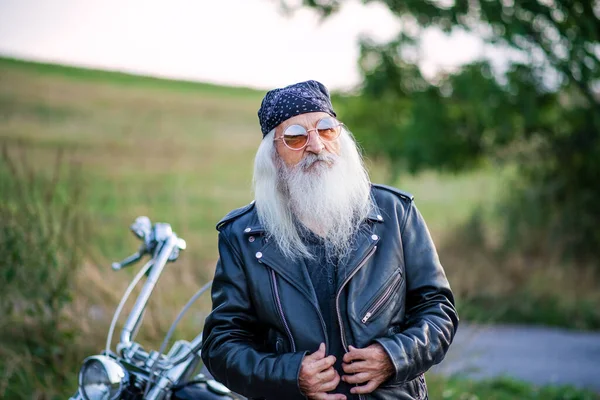 Homem idoso viajante com moto e óculos de sol no campo . — Fotografia de Stock