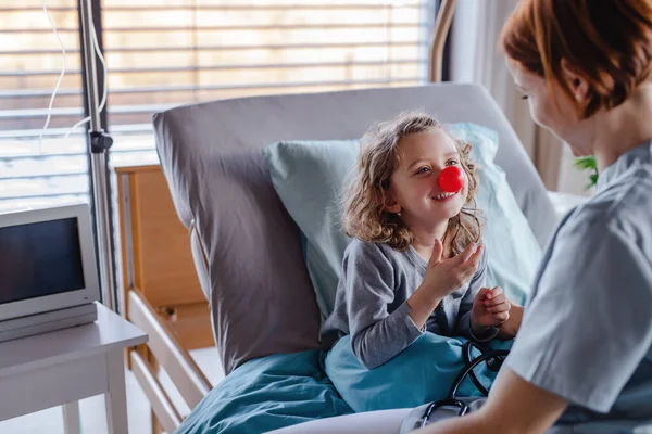 Amable médico femenino examinando niña pequeña en la cama en el hospital . — Foto de Stock