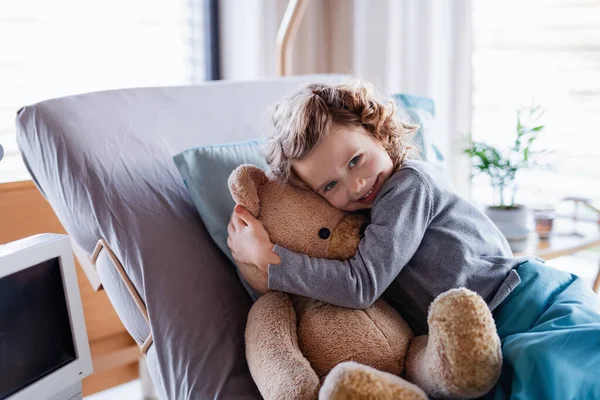 Улыбающаяся маленькая девочка с плюшевым мишкой в постели в больнице . — стоковое фото