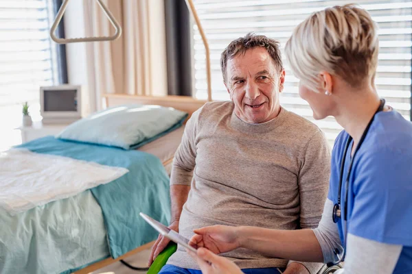 Um profissional de saúde e paciente idoso em cadeira de rodas no hospital, conversando . — Fotografia de Stock