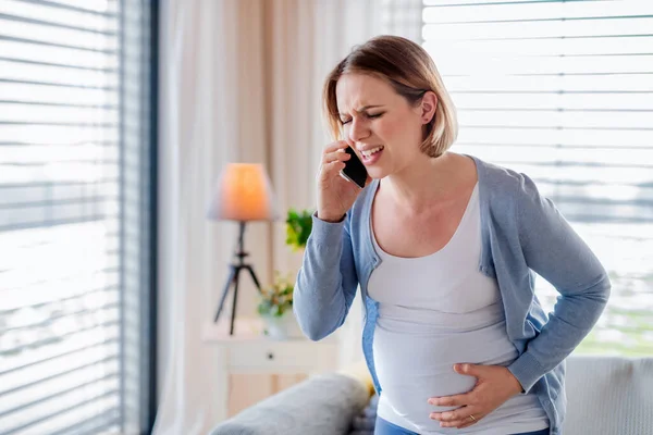 Portret kobiety w ciąży cierpiącej w domu, wykonującej telefon alarmowy. — Zdjęcie stockowe