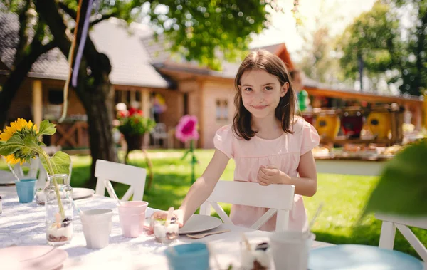 Porträtt av liten flicka stående vid bordet utomhus i trädgården på sommaren på fest. — Stockfoto