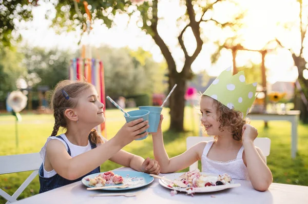 Małe dziewczynki siedzące przy stole na letniej imprezie ogrodowej, koncepcja uroczystości urodzinowych. — Zdjęcie stockowe