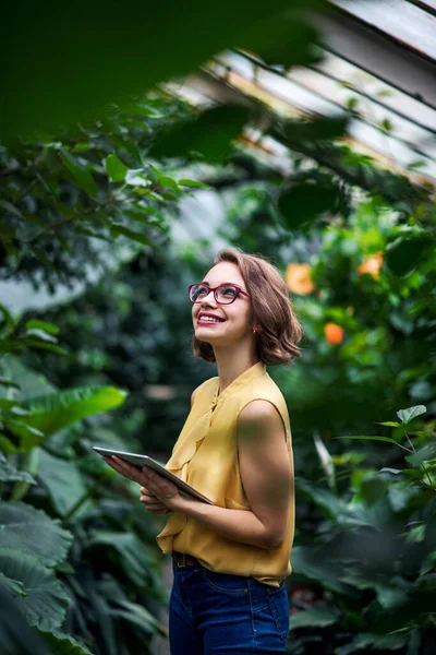 Mujer joven con tableta de pie en el jardín botánico. Copiar espacio . — Foto de Stock