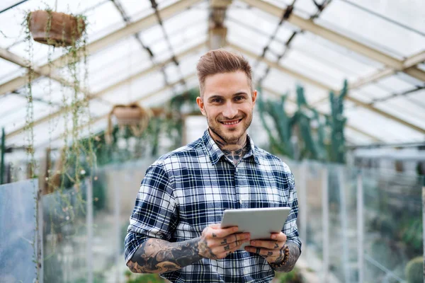 Man researcher standing in greenhouse, using tablet.