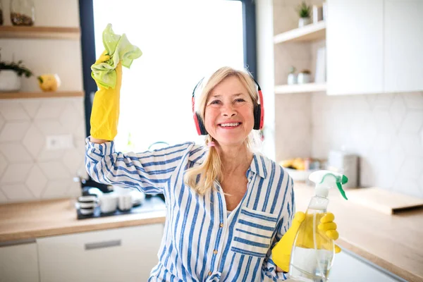 Portrait of senior woman with headphones and gloves cleaning indoors at home. — Stock Photo, Image