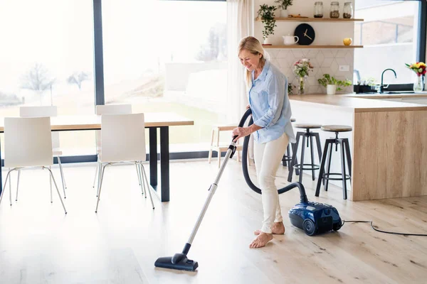 Portrait of senior woman with vacuum cleaner indoors at home, hoovering. — Stock Photo, Image