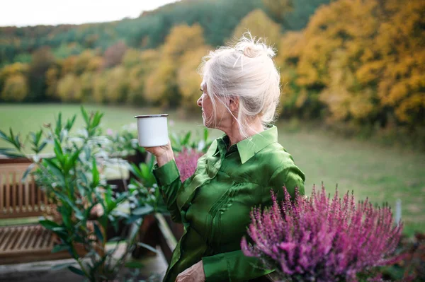 Seniorin mit Kaffee steht draußen auf der Terrasse und ruht sich aus. — Stockfoto