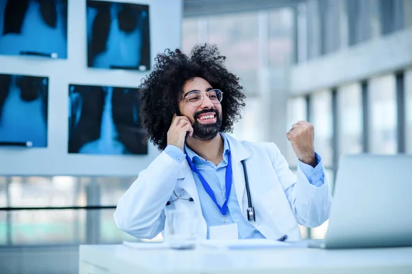 Porträtt av manlig läkare sitter på sjukhus, med hjälp av laptop och smartphone. — Stockfoto