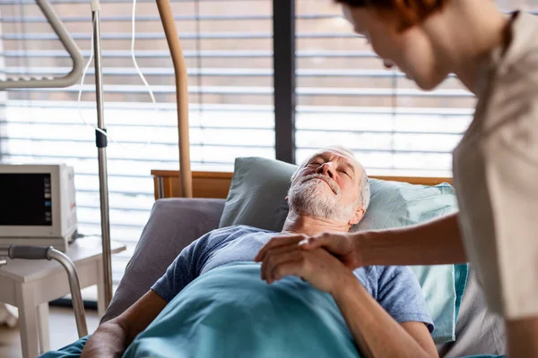 Oigenkännlig kvinnlig läkare undersöker äldre patient i sängen på sjukhus. — Stockfoto