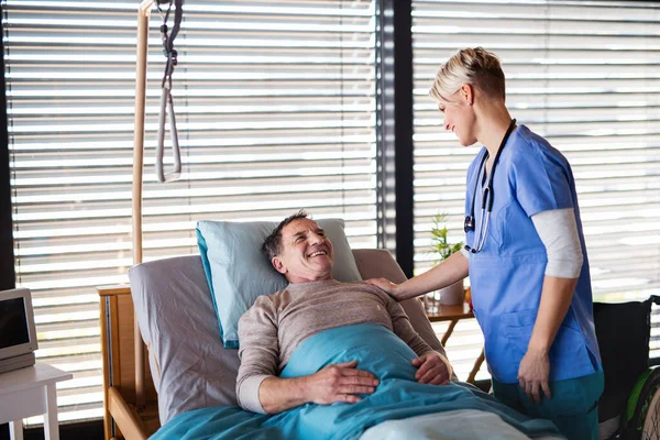 Υγειονομικός λειτουργός ή νοσηλευτής που απευθύνεται σε ηλικιωμένο ασθενή στο κρεβάτι του νοσοκομείου. — Φωτογραφία Αρχείου
