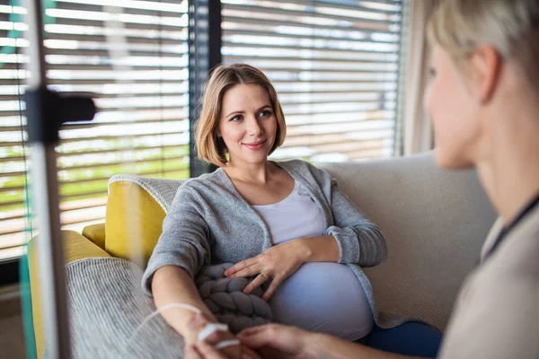 Gezondheidszorgverlener met infuus dat zwangere vrouw thuis onderzoekt. — Stockfoto