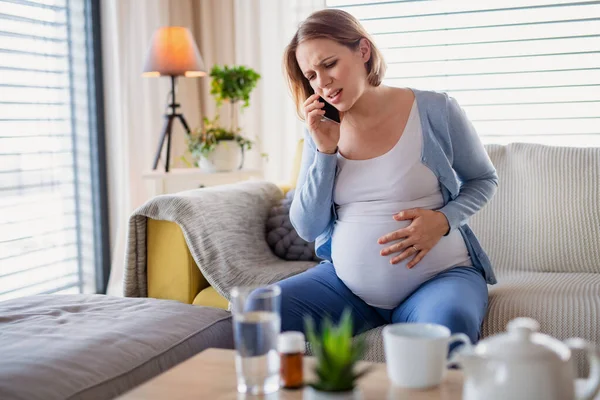 Porträt einer schwangeren Frau, die zu Hause Schmerzen hat und einen Notruf absetzt. — Stockfoto