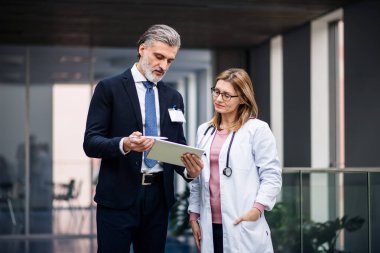 İlaç satış temsilcisi elinde tabletle doktorla konuşuyor..