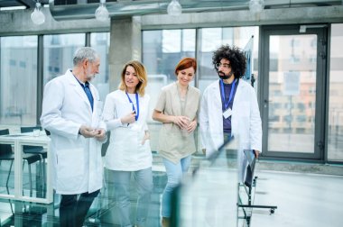 Konferansta koridorda yürüyen bir grup doktorun ön görüntüsü.